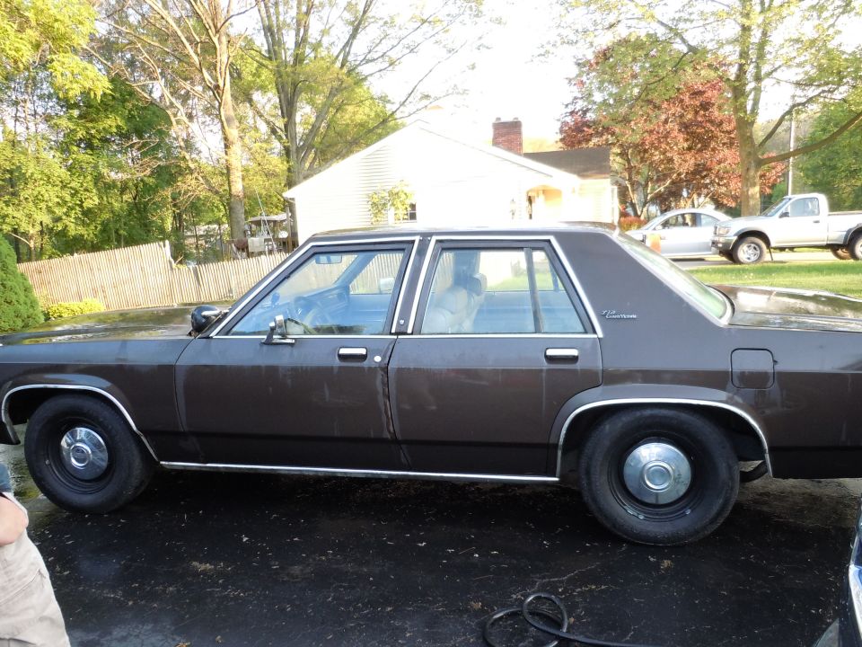 Brown Ford sedan parked on wet asphalt, with a silver pickup truck and car in the background