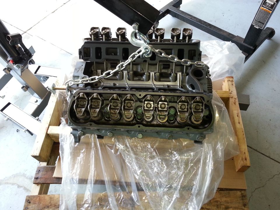 Engine on wooden pallet, suspended by chain and engine hoist