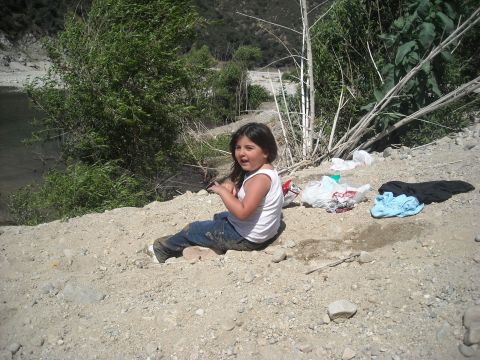 1988 Ford Bronco - A young girl sits on a dirt embankment near a river, with discarded clothing and trash scattered around her.