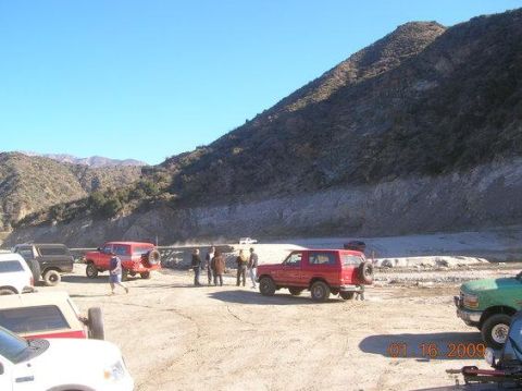1988 Ford Bronco - A group of people stand near several SUVs, including a red 1988 Ford Bronco, in a dusty outdoor area.