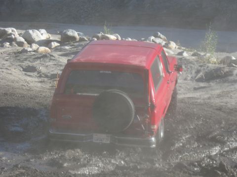 1988 Ford Bronco - Red 1988 Ford Bronco is stuck in muddy terrain, seen from the rear.