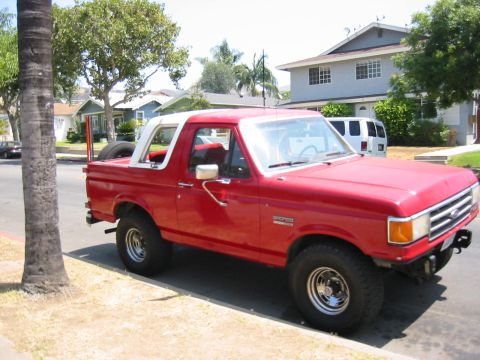 1988 Ford Bronco - This red 1988 Ford Bronco is parked curbside in a neighborhood with houses in the background.