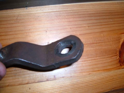1988 Ford Bronco - A close-up view of a metal automotive component, likely a bracket or linkage, displayed on a wooden background. The Supermotors.net waterma…