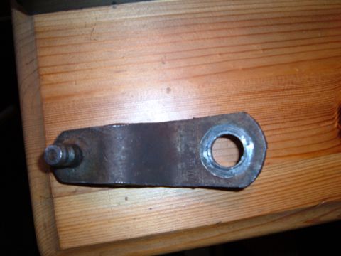 1988 Ford Bronco - Close-up of a metal linkage part with a pin and a hole, placed on a wooden surface.