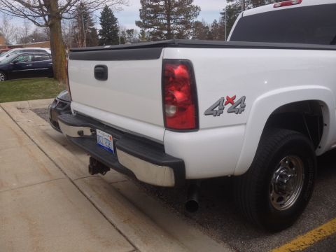 2006 Chevrolet Silverado 2500 - The rear of a white Chevrolet Silverado pickup truck is shown, a chrome bumper and a 4x4 decal on the fender.