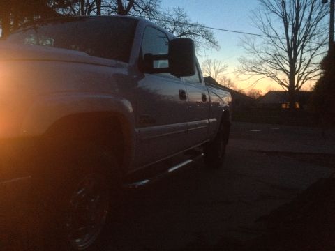 2006 Chevrolet Silverado 2500 - A silver truck is seen from a 3q front angle during dusk, with bare trees and houses in the background.