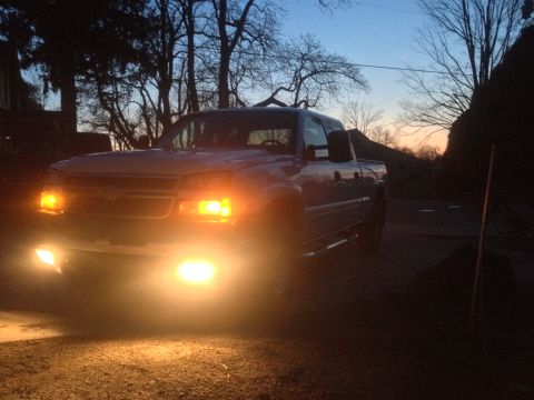 2006 Chevrolet Silverado 2500 - A blue pickup truck is parked outside at dusk, its lights illuminated against the darkening sky.