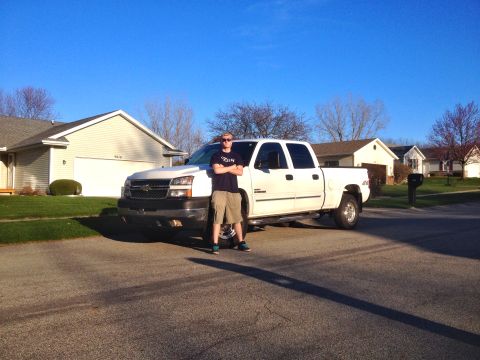 2006 Chevrolet Silverado 2500 - A man stands in front of a white 2006 Chevrolet Silverado 2500 pickup truck on a sunny day in a suburban neighborhood.