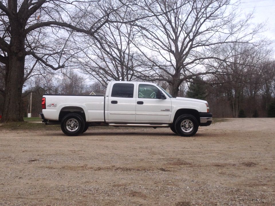 White 2006 Chevrolet Silverado 2500 pickup truck, crew cab, long bed, parked on gravel lot with trees in background