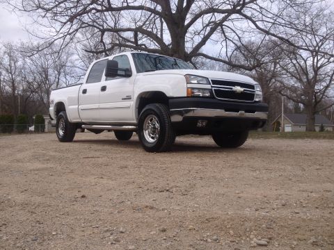 2006 Chevrolet Silverado 2500 - A white 2006 Chevrolet Silverado 2500 pickup truck is parked on a gravel lot with trees in the background.