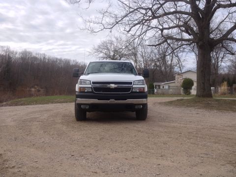 2006 Chevrolet Silverado 2500 - A white Chevrolet pickup truck is parked on a dirt road with trees and houses in the background.
