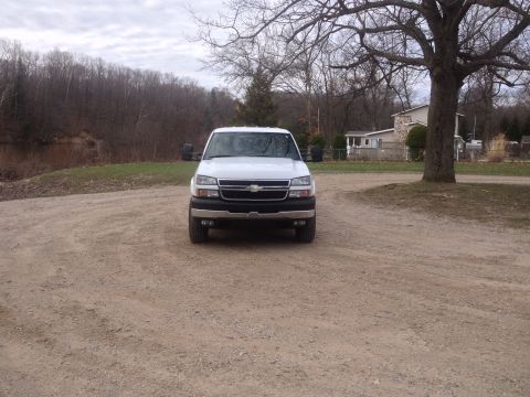 2006 Chevrolet Silverado 2500 - This white 2006 Chevrolet Silverado 2500 is parked on a gravel driveway with a wooded area and houses in the background.