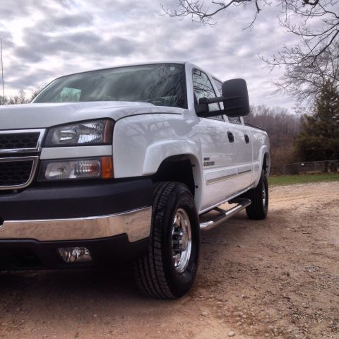 2006 Chevrolet Silverado 2500 - A white 2006 Chevrolet Silverado 2500 pickup truck is parked on a dirt road under a cloudy sky.
