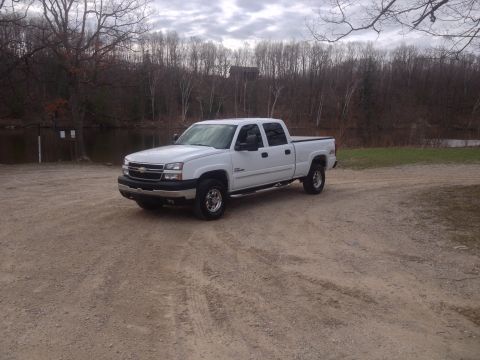 2006 Chevrolet Silverado 2500 - A white 2006 Chevrolet Silverado 2500 pickup truck is parked on a gravel surface with trees and water in the background.