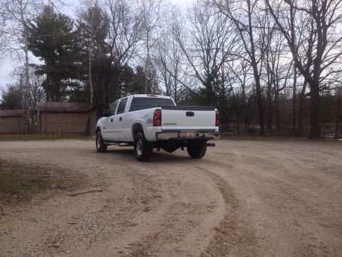 2006 Chevrolet Silverado 2500 - Rear view of a white 2006 Chevrolet Silverado 2500 pickup truck on a dirt lot with trees in the background.