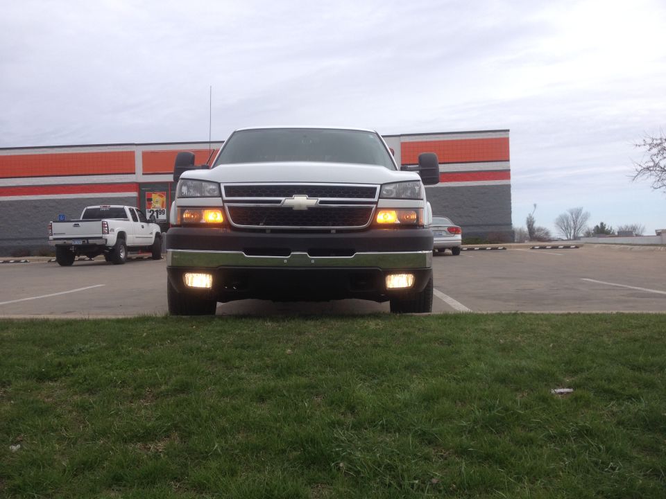 White Chevrolet Silverado 2500 front view, chrome bumper, tow mirrors, parked on grass