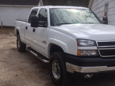 2006 Chevrolet Silverado 2500 - This white pickup truck is parked on a dirt lot next to a building. The truck has a crew cab and dual rear wheels.