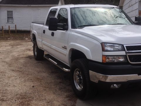 2006 Chevrolet Silverado 2500 - A white pickup truck is parked on a dirt lot in front of a white building.