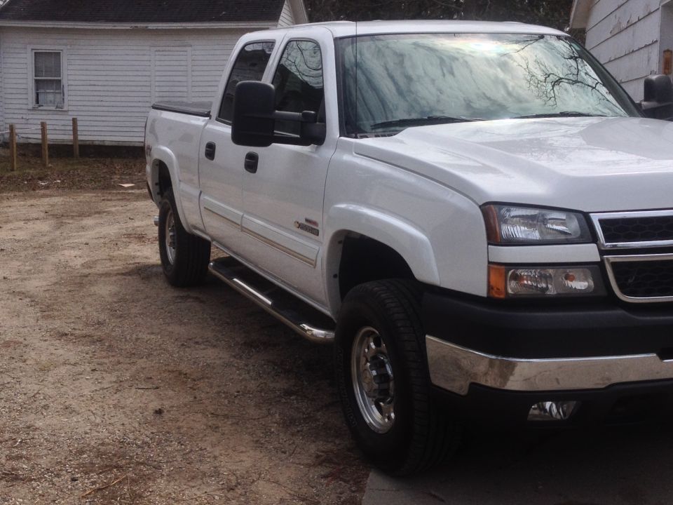 White pickup truck with chrome side steps and tow mirrors, parked on a dirt lot