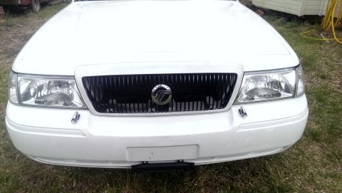 2000 Mercury Grand Marquis - The front of a white Mercury Grand Marquis is shown, a black grille with a chrome emblem and clear headlights.