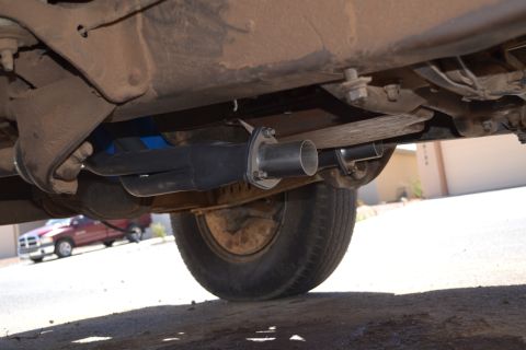1981 Ford F-250 - Underside view of a vehicle's exhaust system and tire, with another red pickup truck visible in the distance.