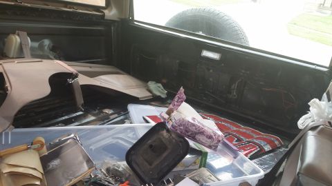 1994 Ford Bronco - The cargo area of a vehicle is cluttered with various parts and storage containers, including a spare tire.