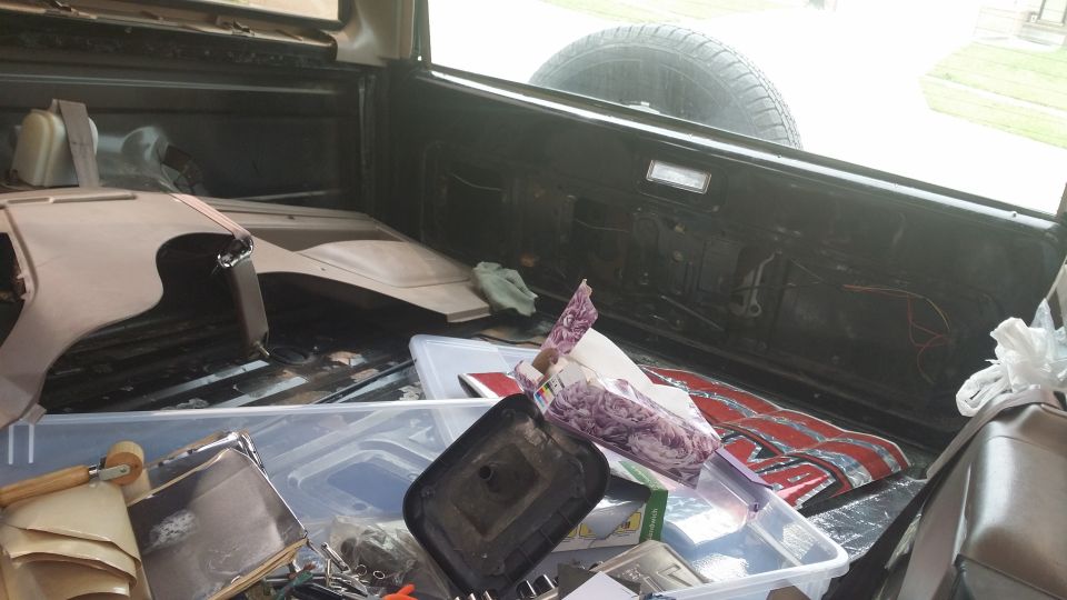 Interior of a 1994 Ford Bronco cargo area filled with parts and storage bins. Spare tire visible