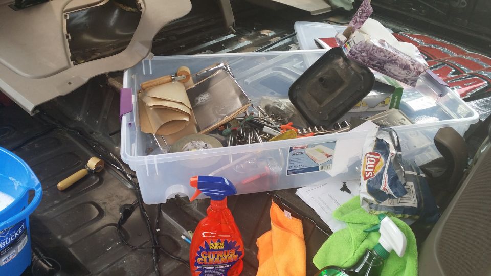 Interior of a vehicle's cargo area with a clear storage bin filled with tools, cleaning supplies, and snacks