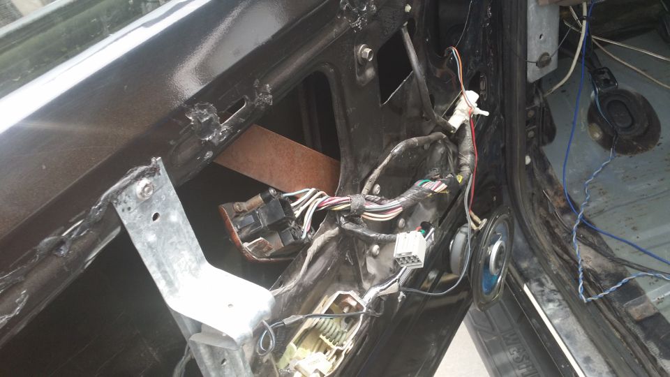 Car door interior with exposed wiring, speaker, and metal bracket