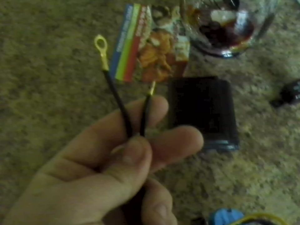 Hand holding two black electrical wires with gold ring terminals