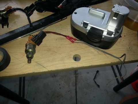 1994 Ford Bronco - A fuel injector and a battery pack are laid out on a wooden workbench, possibly for repair or replacement.