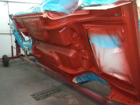 1967 Ford Mustang - Undercarriage of a car is being painted red while on a rotisserie lift.