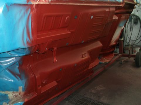 1967 Ford Mustang - The underside of a car is being painted red, with blue sheeting protecting parts of the bodywork.