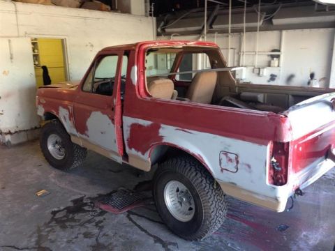 1989 Ford Bronco - This red Ford Bronco is undergoing bodywork, with primer visible on its doors and fenders.