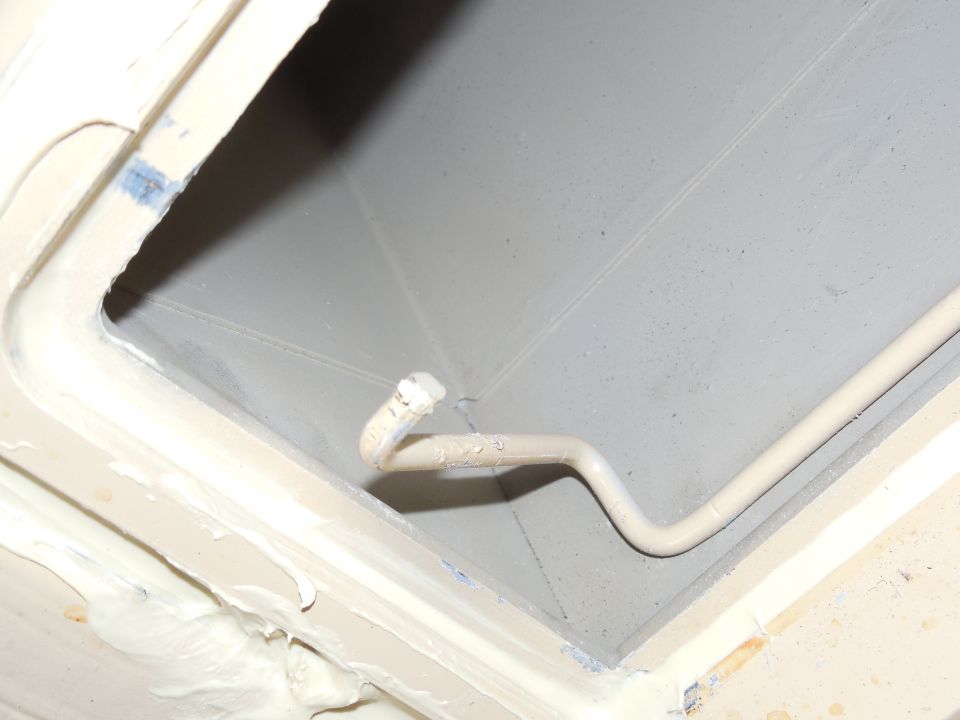 Gray recessed compartment with routed tan cable and white sealant on beige metal edges