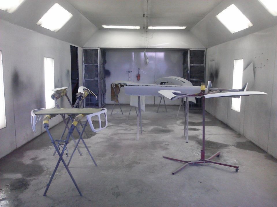 Car body parts on stands in a paint booth, some primed, some disassembled