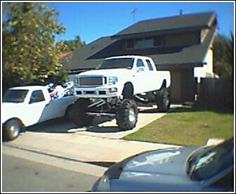 1992 Ford Bronco - A heavily modified pickup truck dominates the driveway, dwarfing a second vehicle parked beside it.