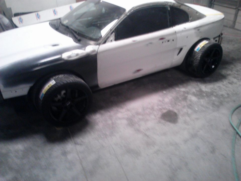 1996 Ford Mustang body in primer and white, with aftermarket wheels and tires, undergoing bodywork