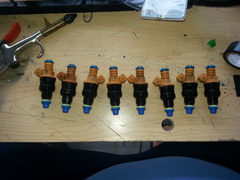 1994 Ford Bronco - A set of eight fuel injectors are displayed on a workbench, alongside a pneumatic tool.