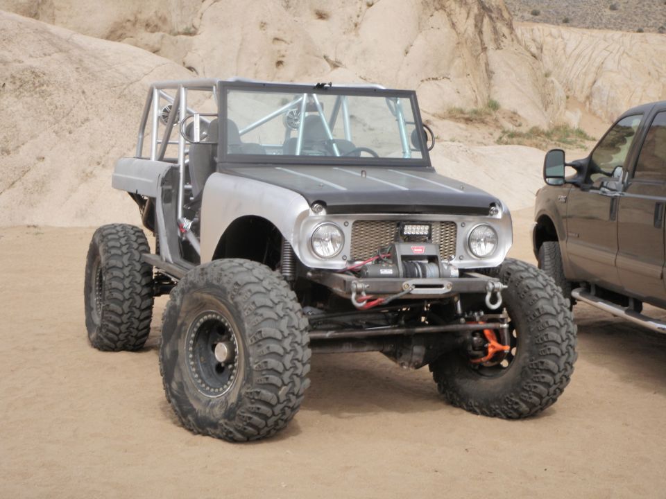 Custom buggy with roll cage and large tires next to a pickup truck in a desert landscape