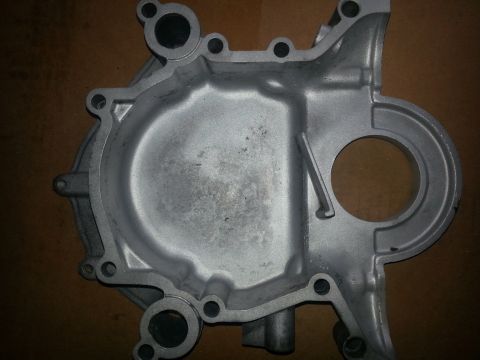 1994 Ford Bronco - Cast aluminum engine front timing cover with bolt holes and crankshaft seal opening resting on cardboard.