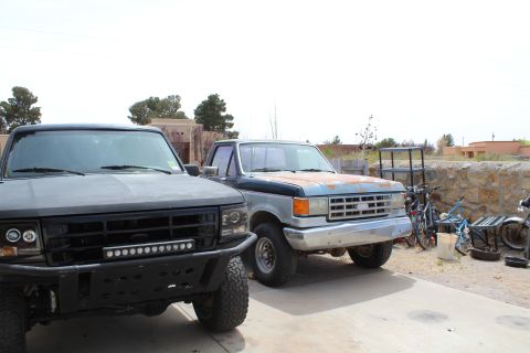 1995 Ford Bronco - A pair of trucks are visible in a yard with various other items like bicycles and a motorcycle.