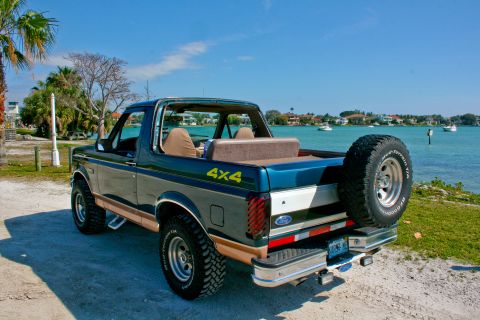 1994 Ford Bronco - Ford Bronco with removable top and 4x4 decal parked near a body of water with boats.