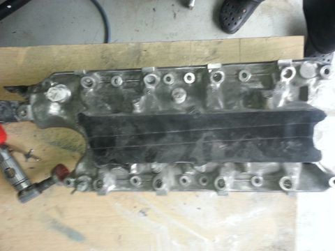 1994 Ford Bronco - An engine intake manifold is shown on a wooden surface, possibly undergoing maintenance or repair.