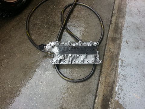 1994 Ford Bronco - An engine intake manifold rests on a wet concrete surface next to a coiled black hose.
