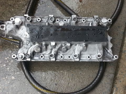 1994 Ford Bronco - A metal engine intake manifold is shown, possibly being cleaned, with visible bolts and text markings.