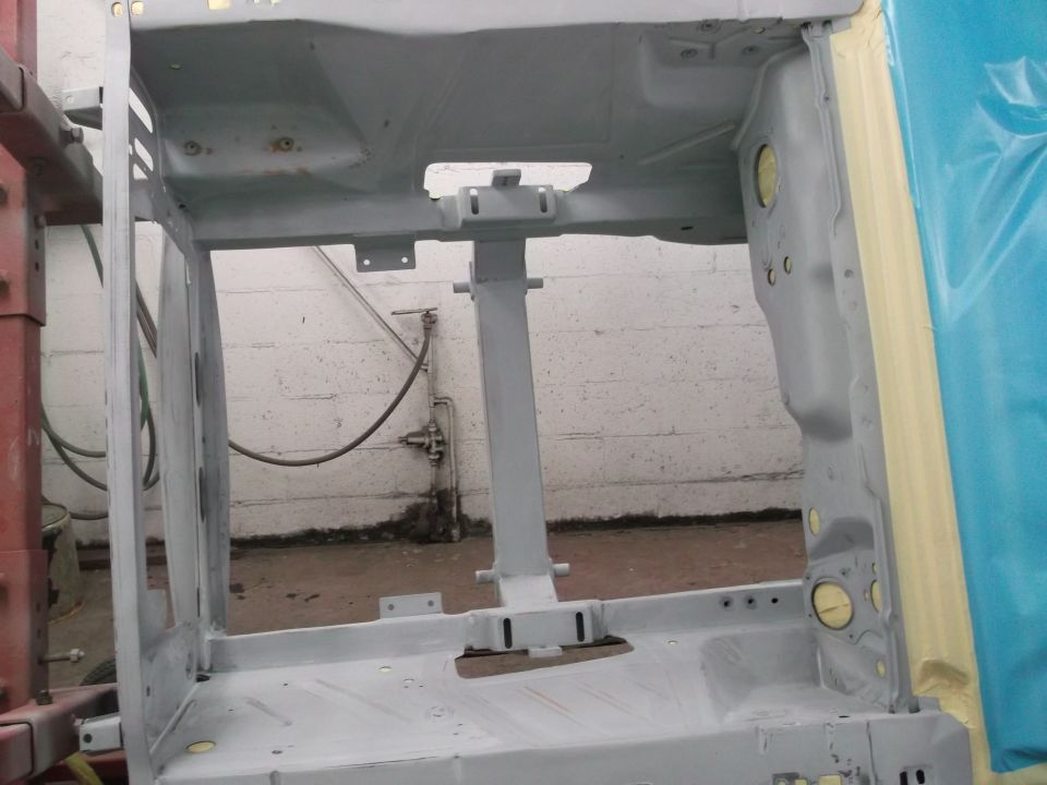 Car frame stripped down and primed, possibly for restoration. Shows internal structure and mounting points