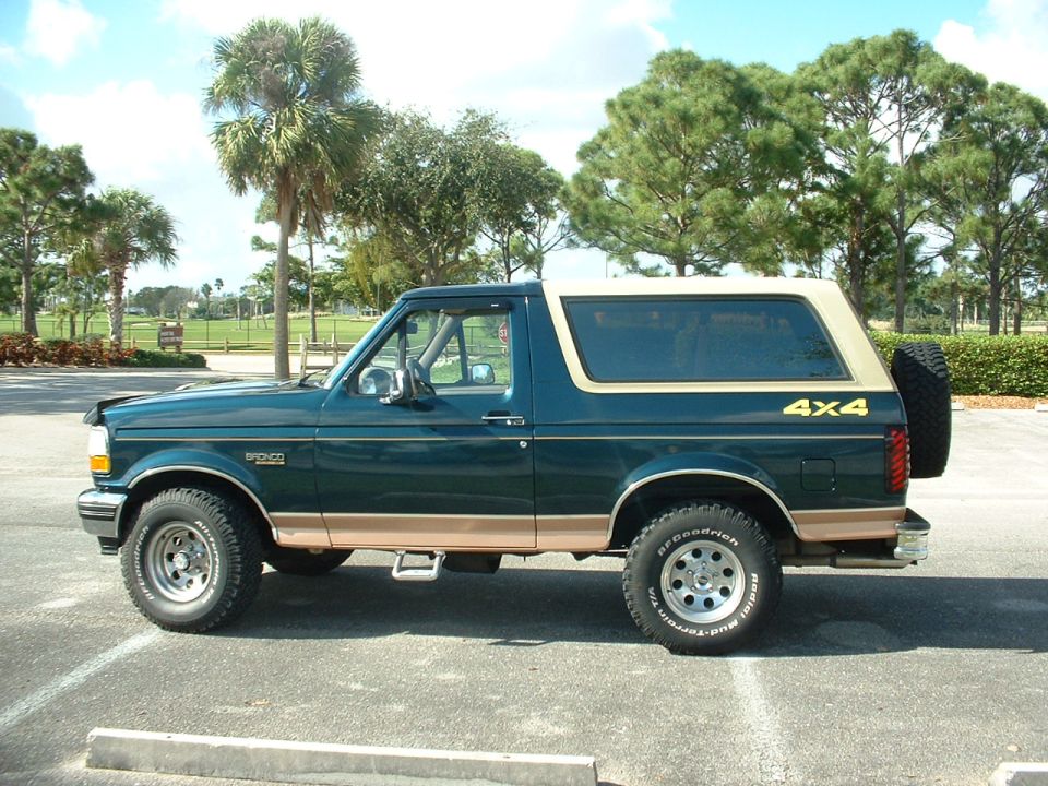 Green and tan Ford Bronco SUV with a spare tire mounted on the rear, seen from the side