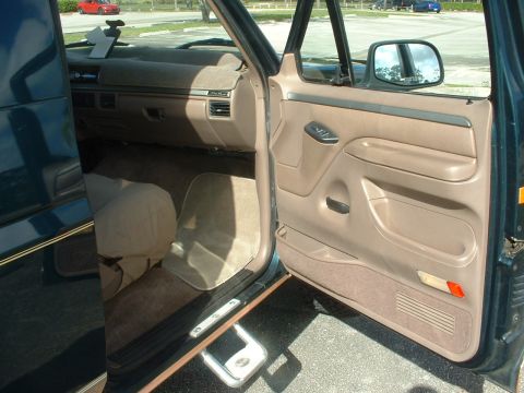 1994 Ford Bronco - The interior of a dark green SUV shows beige seats and door panels. The exterior is visible through the open door and side mirror.