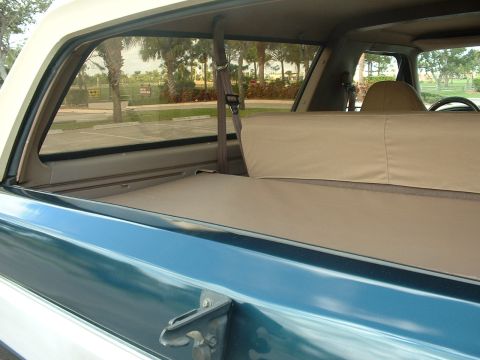 1994 Ford Bronco - The interior of a blue and white SUV is visible, showing the rear cargo area with tan seats and a seatbelt.